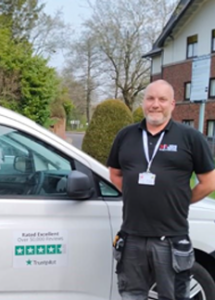 A 24|7 home rescue gas safe engineer is smiling and standing in front of a 24|7 vans